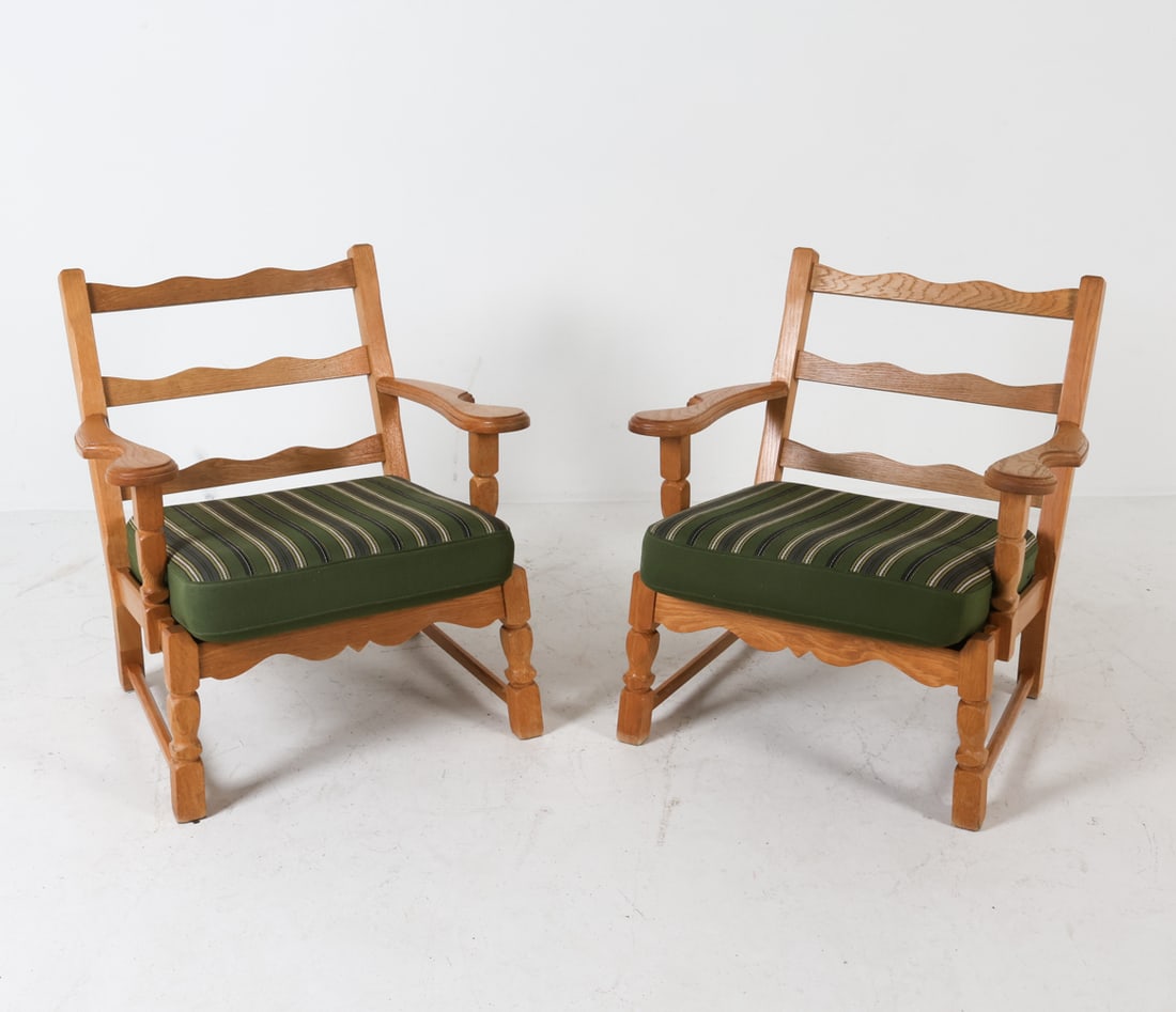 PAIR OF KJAERNULF STYLE DANISH OAK LOUNGE CHAIRS: Carved oak armchairs features adder back designs with wide armrests and green striped wool seat cushions. Dimensions: H 30 x W 27.5" x D 29", SH 16.5" Condition: The underside of one chair has torn fa