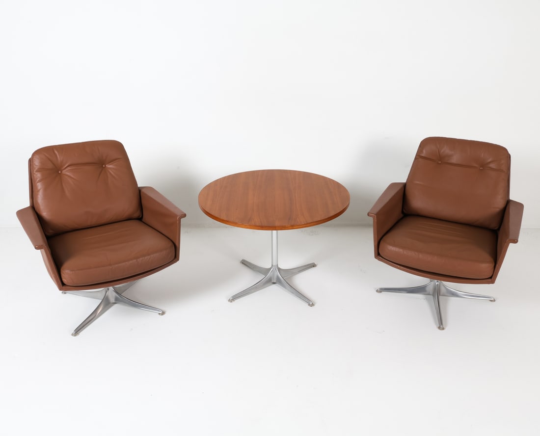 HORST BRUNING FOR COR 'SEDIA' CHAIRS & TABLE SUITE: A pair of 'Sedia' chairs by Horst Bruning for COR, upholstered in tan leather with steel swivel bases, accompanied by a matching table. Dimensions: Chairs H 31.5" x W 28" x D 23.5" x SH 16.5". Table:
