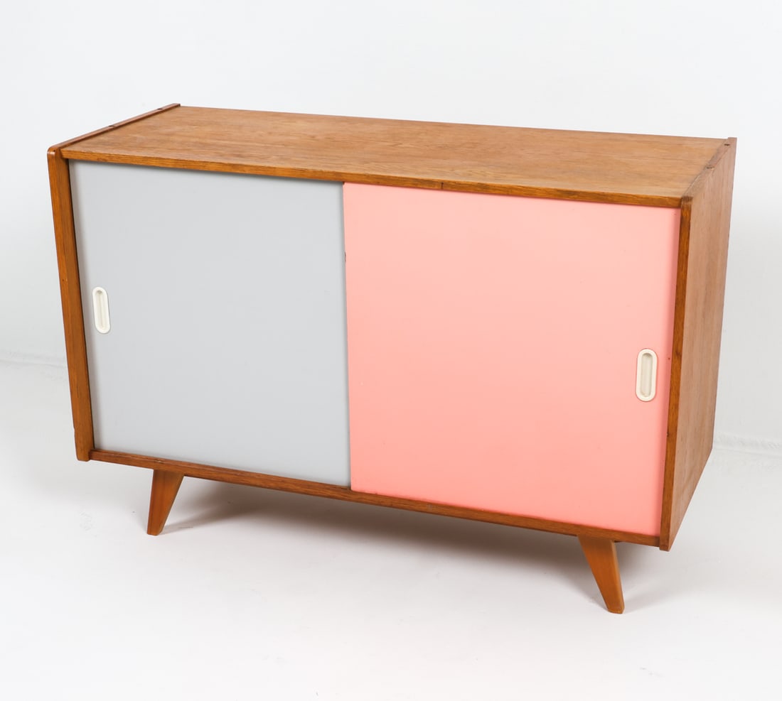 JIRI JIROUTEK MODEL U-452 OAK CABINET C. 1960S: Oak cabinet with two-tone lacquered wood sliding cabinet doors. Adjustable shelves. Dimensions: H 30" x W 43.5" x D 17.75". Condition: Sun fading and some water stains to top. Minor scuffs and scratch