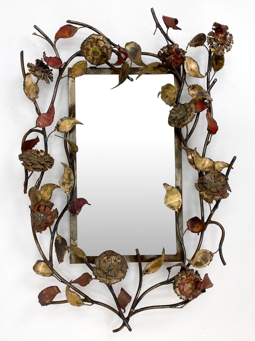 SILAS SEANDEL SCULPTURAL FLORAL MIRROR: Sculptural torch-cut mixed metal floral mirror by Silas Seandel. Signed and dated 1991 on a stem near the bottom. Copper, brass, and steel. Dimensions: H 44" x W 29" x D 6.5" Condition: Light surface
