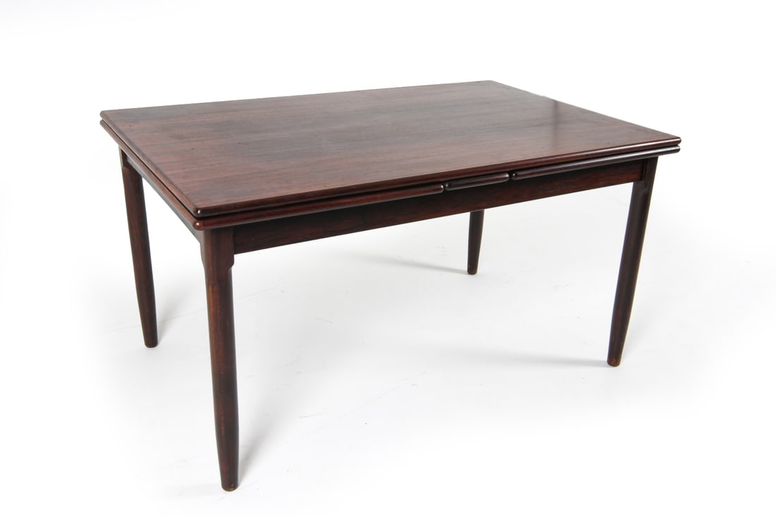 J. L. MOLLER ROSEWOOD EXTENDING DINING TABLE 1960S: (2) Leaves included, stored within table. Dimensions: H 29.75" x W 54.5" x D 35.5". Leaf W 23.75". Condition: Minor scuffs and dings to legs. Wear consistent with age and use. sun fading to surface JB