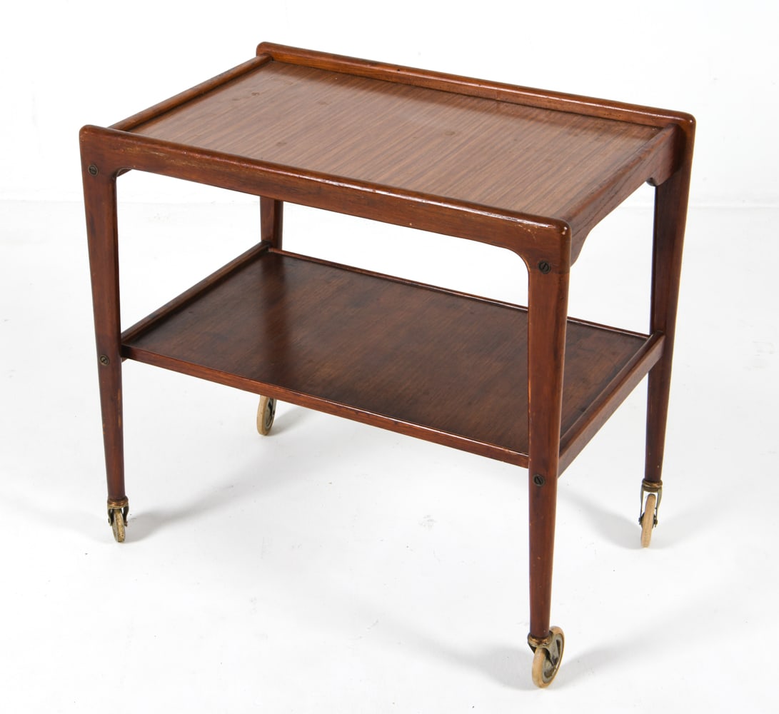 YNGVE EKSTROM STYLE SWEDISH BAR CART C. 1960S: On brass casters. Dimensions: H 24.25" x W 25.5" x D 16.5" Condition: Water rings to lower shelf. Scattered scratches and surface scuffs. Wear consistent with age and use.