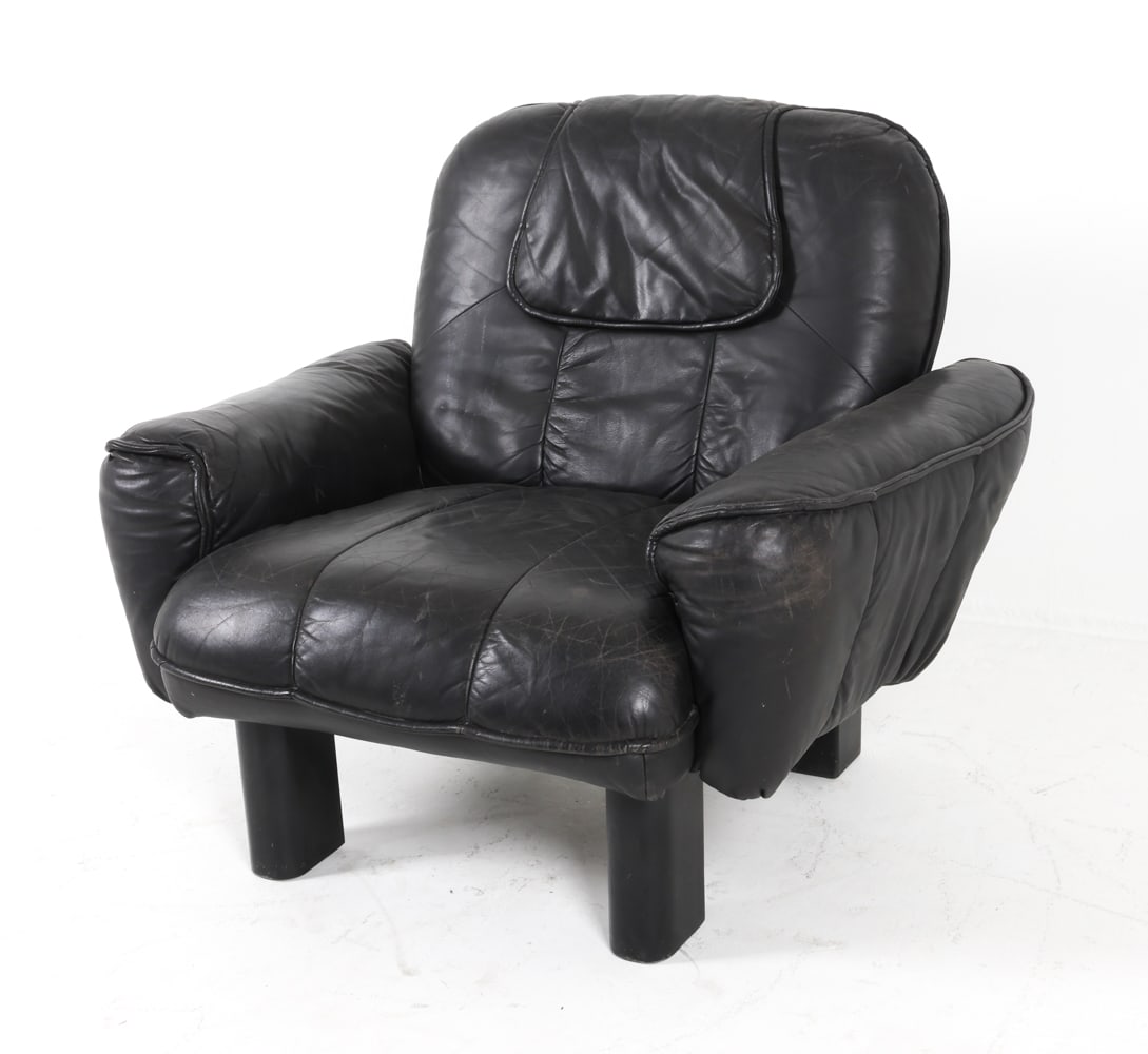 DE SEDE STYLE LEATHER LOUNGE CHAIR C. 1970S: Black-tone leather upholstery and black painted oak feet. Dimensions: H 33" x W 41" x D 30", SH 16" Condition; Moderate scuffs and creases to leather. Rubbing to outer edges. Moderate nicks and scratc