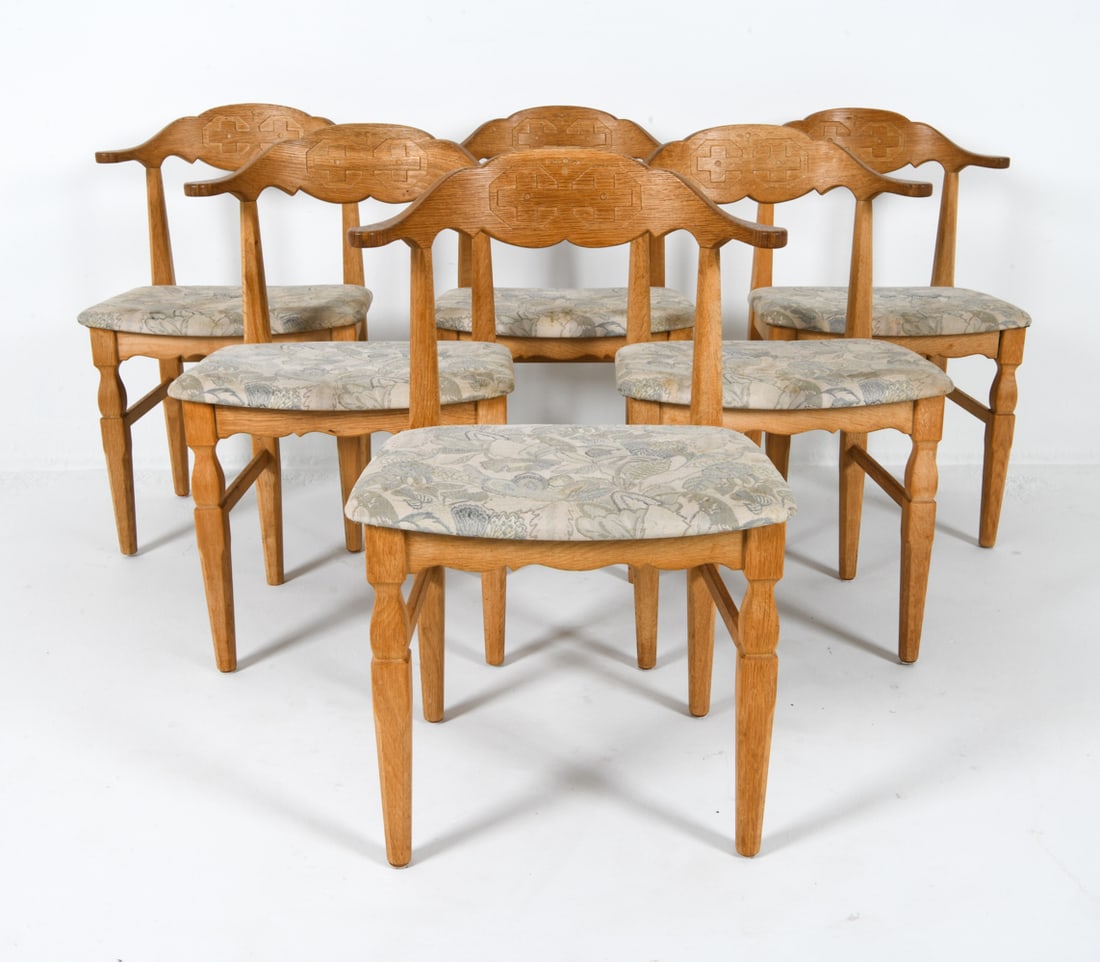 (6) HENNING KJAERNULF DANISH OAK DINING CHAIRS: Oak frames with carved decoration. Botanical fabric upholstered seats. Denmark, circa 1970s. Dimensions: H 31" x W 21.25" x D 18" x SH 17.5". Condition: Some discolored spots to fabric. Faint water sp