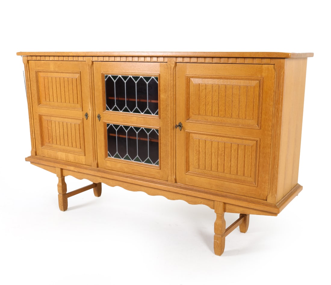 HENNING KJAERNULF DANISH OAK SIDEBOARD C. 1970S: Soldered stained glass center cabinets. Includes (1) Key. Adjustable shelves. Dimensions: H 46.5" x W 80.25" x D 17.5" Condition: Water marks to interior shelves. Slight musty odor to interior cabinet
