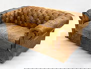 CHESTERFIELD STYLE LEATHER LOVESEAT C. 1960S: Brown tufted leather upholstery. Beech legs. Dimensions: H 27" x W 61" x D 33" x SH 16.5". Condition: Some drying to leather, fading and discoloration to seat and arms. Tobacco odor. Wear consistent w