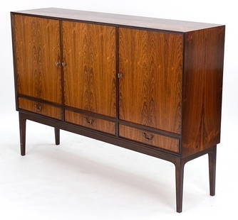 MANNER OF SEVERIN HANSEN DANISH ROSEWOOD SIDEBOARD: Scandinavian three-door high board with shelves inside. Brass handles. One cabinet features 3 small storage drawers. Unmarked Dimensions: H 45.5" x W 65" x D 16.25" Condition: Wear consistent with age