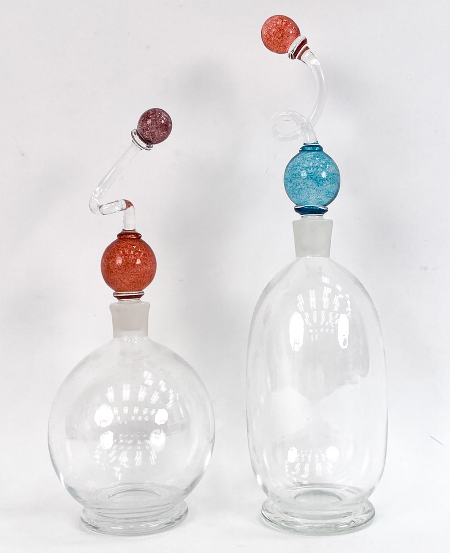 PAIR OF BOB CROOKS 'COLOUR BALL' DECANTERS: Pair of glass decanters with spiral stoppers with colored balls. Both signed on undersides and each numbered 744 and 743. Dimensions: (Taller) H 15" x Dia 3.75" Condition: Couple scratches to undersid