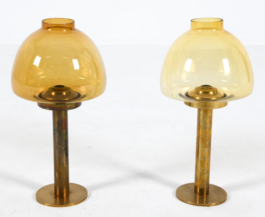 PAIR HANS AGNE JAKOBSSON BRASS CANDLE HOLDERS: Unmarked. Brass posts with amber glass shades. Dimensions: H 13.5" x Dia. 6.75" Conditions: Presents well overall, a few minor scuffs and rubs to stand, minor fleabite nick to one shade DDE C