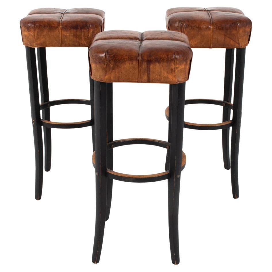 (3) LEATHER STOOLS IN THE STYLE OF MICHAEL THONET: This set of (3) Art Deco stools have a dignified air about them, a lasting remnant of the time when they were made nearly a century ago. With subtly flared beech carved legs in a manner not dissimilar
