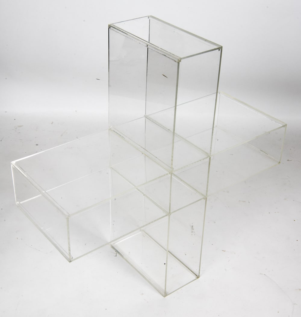 MODERNIST LUCITE CROSS FORM BOOKCASE: Lucite/Acrylic bookcase/magazine rack. Apparently unmarked. Dimensions: H 27" x W 27" x D 12" Condition: Scratches, nicks, dings, scuffs. Wear consistent with age and use.