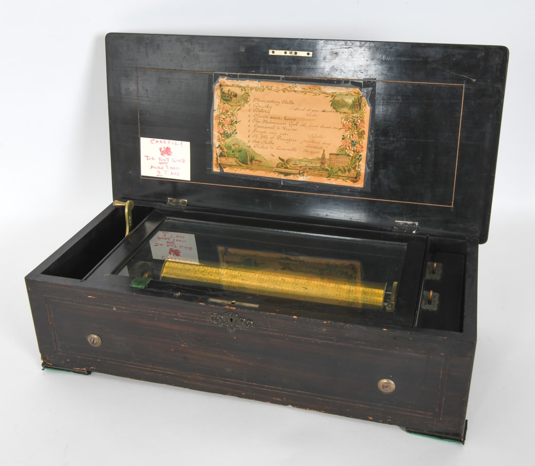 19TH CENTURY ANTIQUE SWISS CYLINDER MUSIC BOX: The music box has a cylinder with pins that pluck a steel comb to produce music. Comes with a list of 10 "airs" that it plays. Made in Zurich. Featuring brass mechanism and wooden box. Carved Lion sym