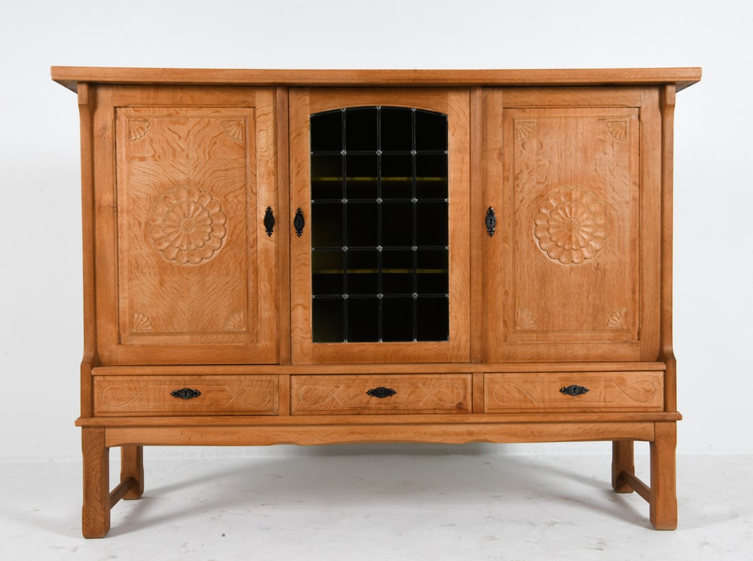 HENNING KJAERNULF DANISH OAK SIDEBOARD C. 1970S: Oak and glass highboard by Henning Kjaernulf. Key included. Carved decoration to cabinet doors and drawer fronts. Glass panels to center cabinet door. Denmark, circa 1970s. Dimensions: H 50" x W 68" x