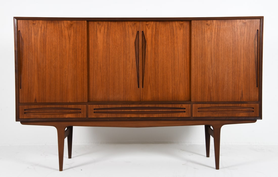 MANNER OF JOHANNES ANDERSON DANISH TEAK SIDEBOARD: Adjustable shelves and sliding cabinet doors. Elongated inset cabinet door pulls. Dry bar to center cabinet with frosted decorated mirror. Felt lined drawers. Denmark, circa 1970s. Dimensions: H 44.25