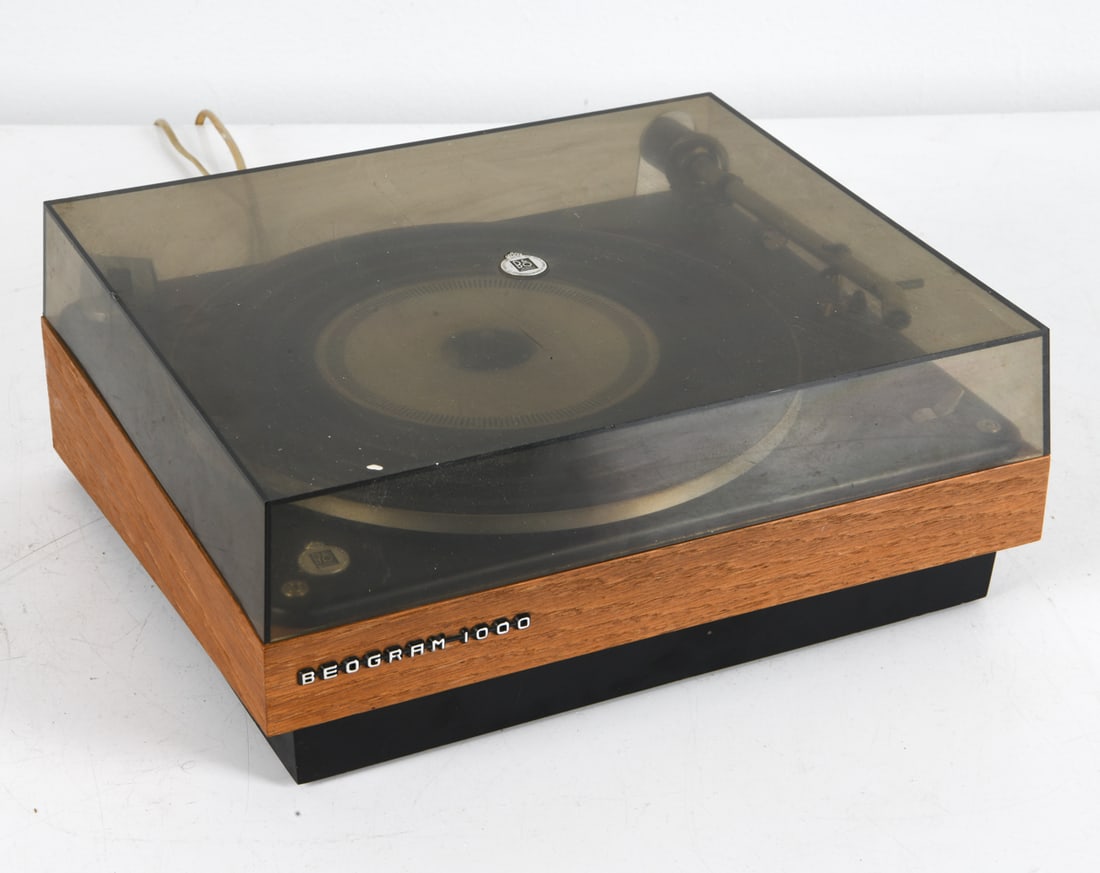 BANG & OLUFSEN BEOGRAM 1000 TURNTABLE C. 1960S: Designed by Jacob Jensen. Teak case. Denmark, circa 1960s. Dimensions: 5.5" x W 14.25" x D 14.25". Condition: Wiring untested, European plug. Scuffs to plastic cover. No needle. Wear consistent with a