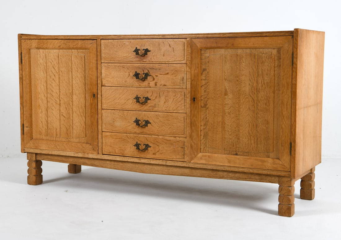 HENNING KJAERNULF STYLE OAK SIDEBOARD C. 1970S: Key included. Felt lined drawers. Adjustable shelves. Brass pulls. Denmark, circa 1970s. Dimensions: H 32" x W 59.5" x D 17.75". Condition: Sun fading to top. Wear consistent with age and use. CLEVG04