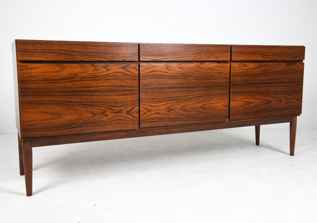 MANNER OF IB KOFOD LARSEN ROSEWOOD SIDEBOARD 1970S: Adjustable shelves. Denmark, circa 1970s. Dimensions: H 32" x W 74.5" x D 19.5". Condition: Ding to center cabinet door corner. Wear consistent with age and use. PERG068