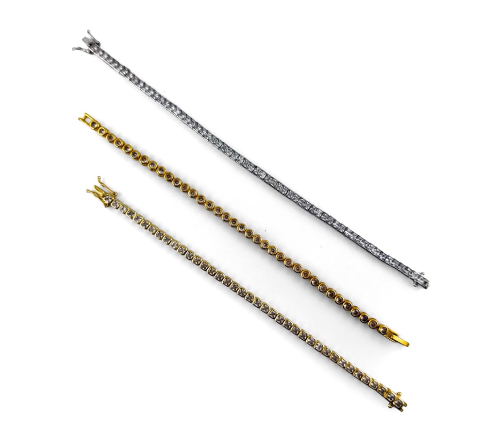 GROUPING OF COSTUME TENNIS BRACELETS: Grouping of three tennis bracelets, two gold-tone and one silver tone. All unmarked. Dimensions: (Largest) L 8" Condition: Light handling wear and scratches consistent with age and use.