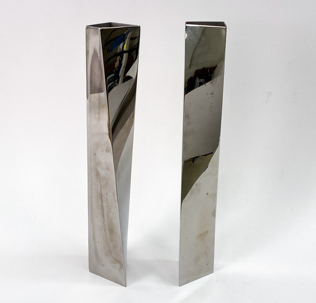 PAIR OF ZAHA HADID ALESSI CREVASSE FLOWER VASES: Contemporary cubist stainless steel vases with twisted shape. Marked underneath. Dimensions: H 16.6" x W 2.5" x D 2.5" Condition: Few scuffs and nicks and light soiling.