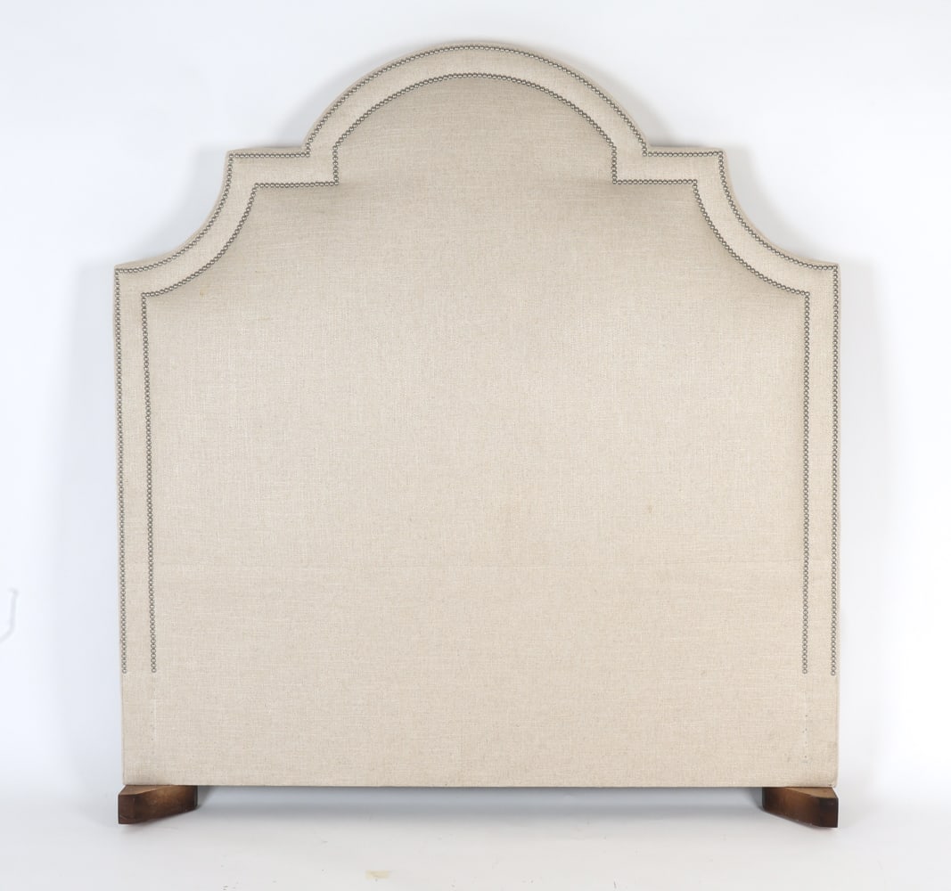 UPHOLSTERED QUEEN HEADBOARD: The shaped headboard with cushioned back embellished with silver nail head trim, upholstered in a woven linen blend fabric, resting on wooden bracket feet. Dimensions: H 71" x W 66" Condition: Some so