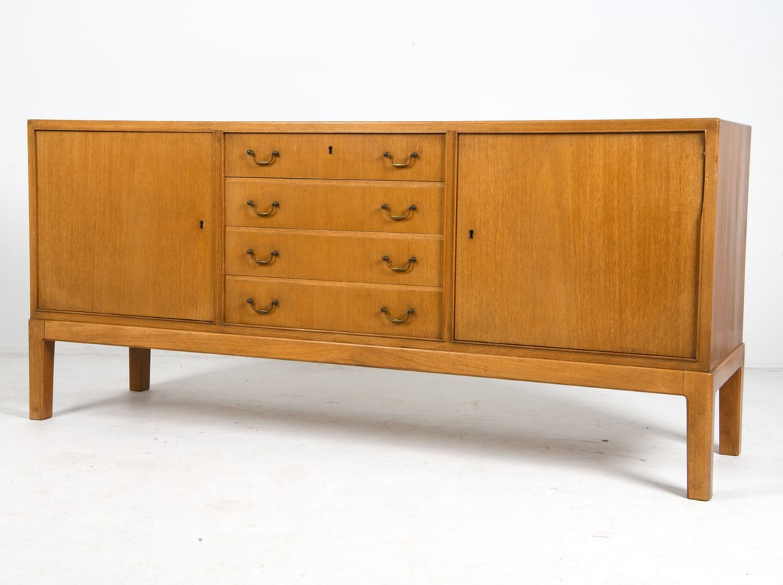 STYLE OF OLE WANSCHER DANISH TEAK SIDEBOARD 1960S: Key included. Removable shelves. Brass drawer pulls. Denmark, circa 1960s. Dimensions: H 32.5" x W 70" x D 19.5". Condition: Lock does not line up with slot to left cabinet. Minor scuffs and scratches