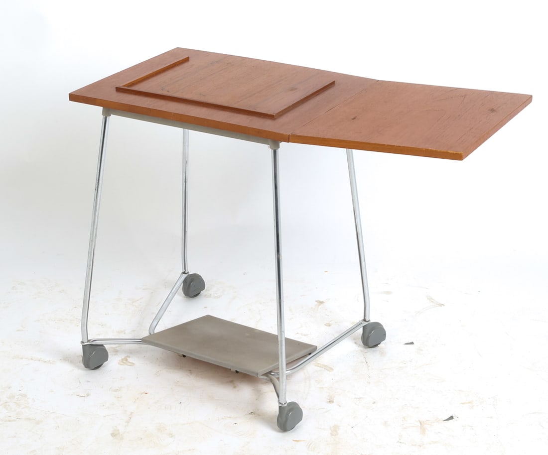 DANISH TEAK TYPEWRITER TABLE CART C. 1970S: Teak typewriter table with (1) drop-leaf. Steel legs with vinyl foot rest. Denmark, circa 1970s. Dimensions: H 25.75" x W 21" x D 19.25". Leaf W 17.75". Condition: Wear consistent with age and use,