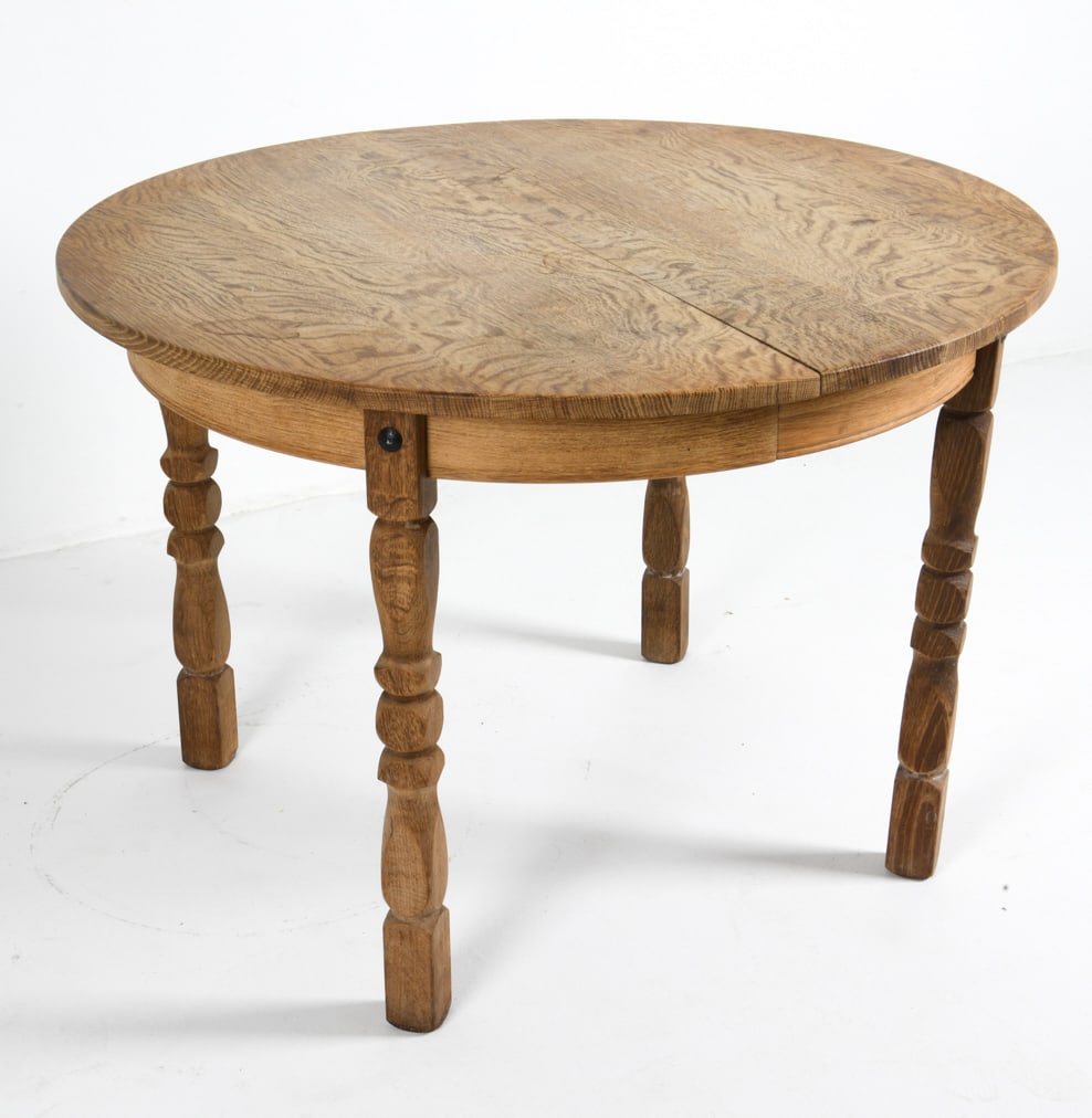 STYLE OF HENNING KJAERNULF DANISH OAK DINING TABLE: (2) Leaves included. Turned legs. Denmark, circa 1970s. Dimensions: H 29" x Diameter 43". Leaves W 19.25". Condition: Fading and surface marks to legs and top. Wear consistent with age and use. Color