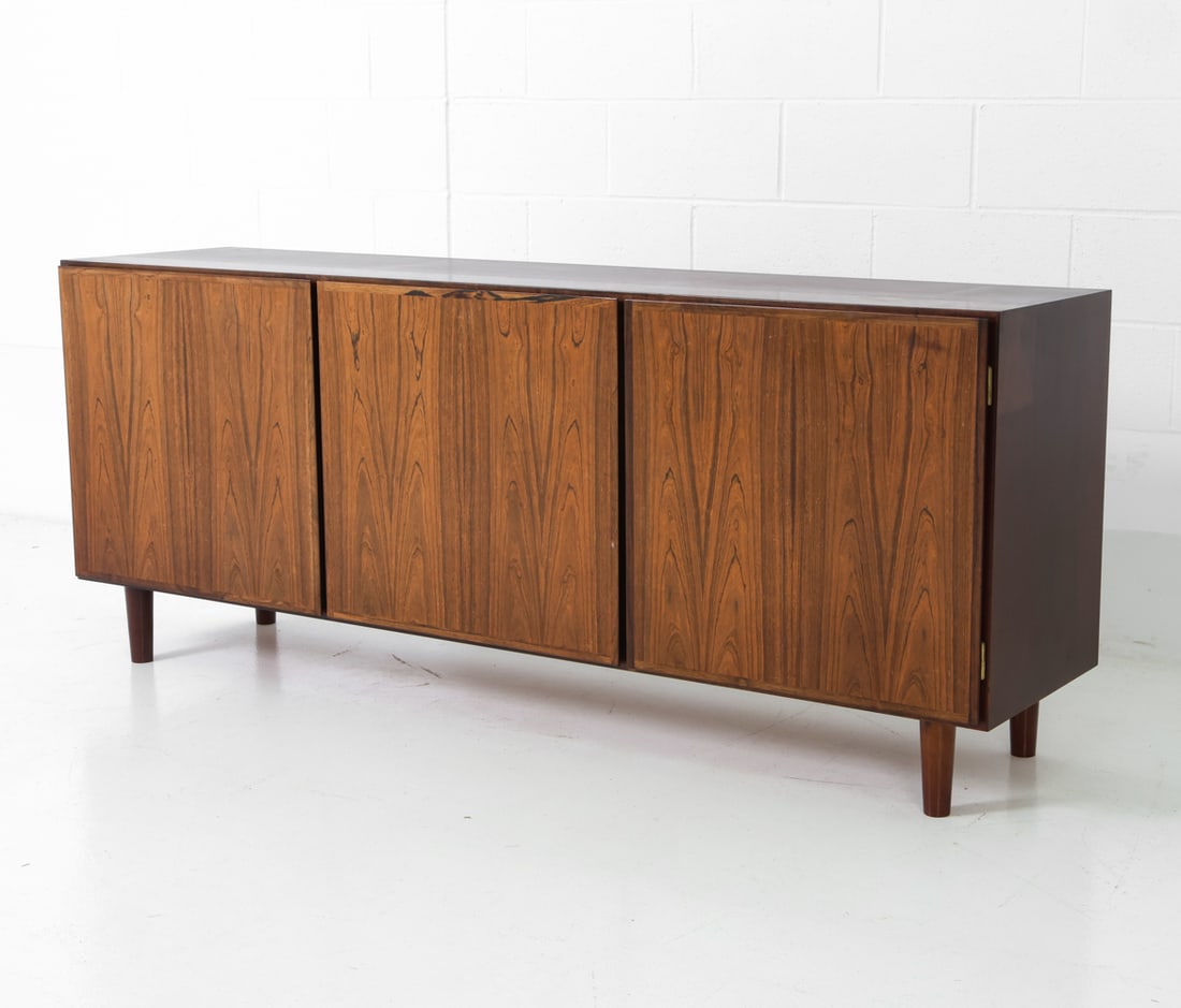 OMANN JUN DANISH ROSEWOOD SIDEBOARD C. 1960S: Three doors with adjustable shelves and two drawers. Apparently unmarked. Denmark, circa 1960s. Dimensions: H 28.75" x W 70.5" x D 17" Condition: Wear consistent with age and use including sun-fading