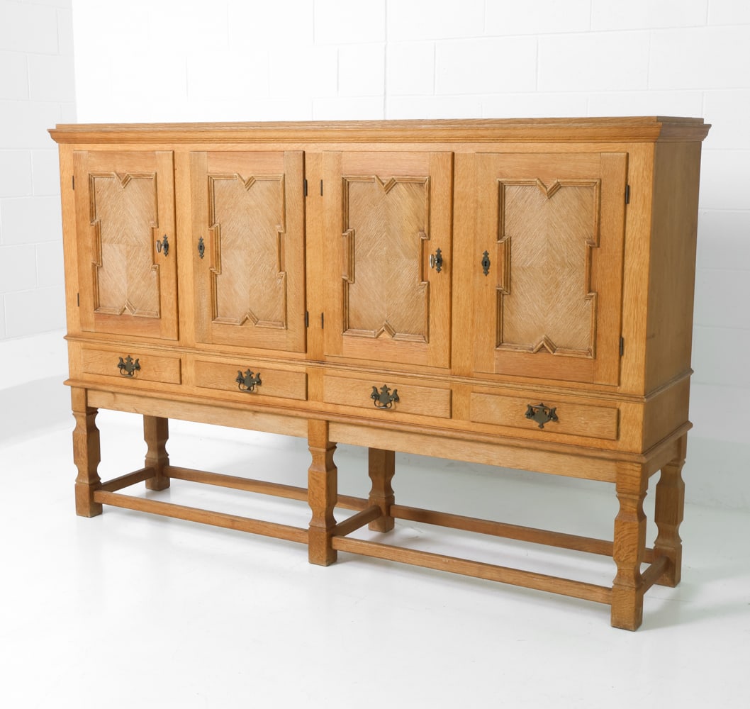 STYLE OF KJAERNULF DANISH OAK SIDEBOARD C. 1970S: Two keys included. Oak frame with carved door panels and brass pulls. Turned legs with stretcher base. Denmark, circa 1970s. Dimensions: H 51" x W 78" x D 18" Condition: Wear consistent with age and