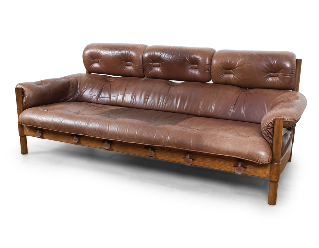 NORELL & ELLEKAER STYLE SWEDISH OAK & LEATHER SOFA: Brutalist leather three-seater sofa in oak frame with exposed wooden slabs and joints. Brown colored leather upholstery and straps. Sweden, circa 1960s. Dimensions: H 33" x W 82" x D 34" x SH 16" Cond