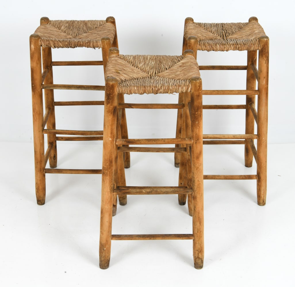 (3) PERRIAND STYLE FRENCH RUSH SEAT BARSTOOLS: Three barstools, with rush seat with ladder foot rest. France, circa 1950s. Dimensions: H 31" x W 13" x D 13" Condition: Some nicks, scratches, and scallop chips to frame. Rubbing to rush. Wear consis