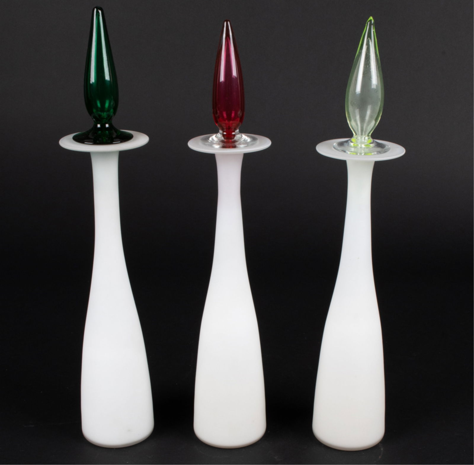 (3) BLEFELD PORTUGAL MODERN ART GLASS BOTTLES: Original "Blefeld & Co." foil labels on 2 of the 3 bottles. Dimensions: H 18.5" x Dia 3.25" Condition: Showing light signs of wear including scuffs to finish and fleabite to tip of one top.