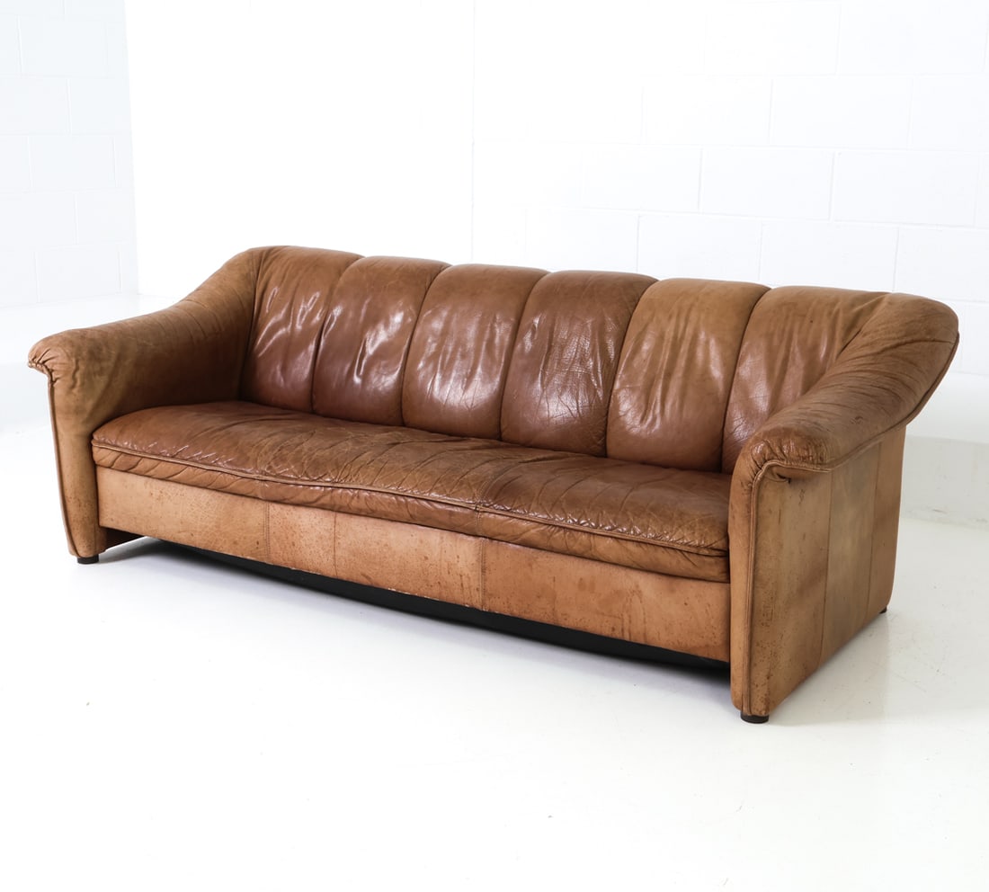 MANNER OF DE SEDE SWISS LEATHER SOFA C. 1970S: Leather upholstery with stitching tufted details to backrest. Swiss, circa 1970s. Dimensions: H 28" x W 80" x D 35" Condition: Wear consistent with age and use. Some discoloration and sun-fading to le