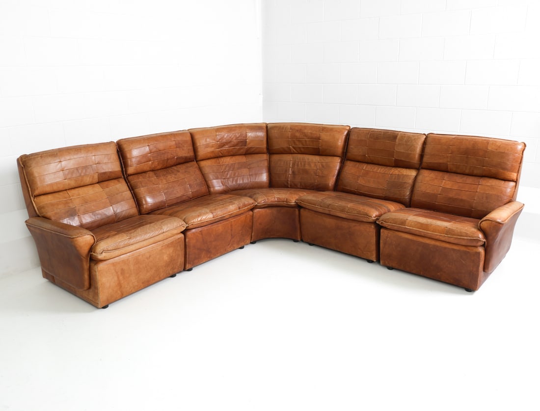DE SEDE STYLE SWISS LEATHER SECTIONAL SOFA C.1970S: (5) Modular sofa in patchwork leather upholstery. Switzerland, circa 1970s. Dimensions: H 34" x W 127" x D 90" x Sh 15.75" Condition: Rubs and scratches to surface of leather, sun-fading present, Wear