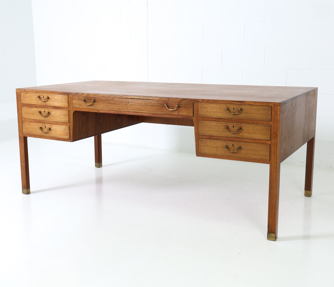 STYLE OF JACOB KJAER DANISH ROSEWOOD DESK C. 1960S: Rosewood writing desk featuring 7 drawers with brass handles. Denmark, circa 1960's Dimensions: H 29" x W 71" x D 35.5" Condition: Some scuffs and sun fading. Wear consistent with age and use. No key.