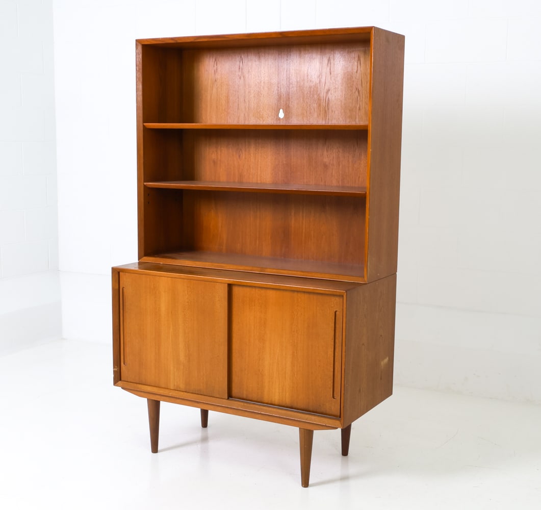 DANISH TEAK BOOKCASE CABINET C. 1960S: Two-piece bookcase cabinet unit, with shelves, two sliding doors and recessed pulls. Denmark, circa 1960's. Dimensions: H 64" x W 39.5" x D 18.5" Condition: Wear consistent with age and use. Scratches