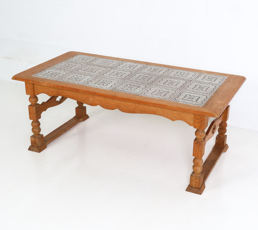 STYLE OF KJAERNULF OAK & TILE COFFEE TABLE C.1960S: Mosaic tile top and carved frame coffee table, in the style of H. Kjaernulf. Denmark, circa 1960's. Dimensions: H 22" x W 56.75" x D 29" Condition: Minor watermarks to top and legs, rubbing, scratches