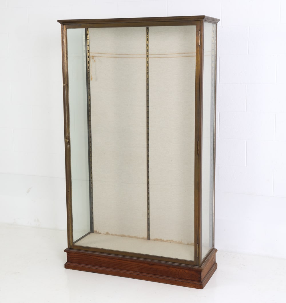 ANTIQUE BRASS AND GLASS VITRINE DISPLAY CASE: A key included. Two door cabinet in brass frame, oak base and glass case cover. Metal brackets for adjustable height to interior. Dimensions: H 65" x W 38" x D 14.5" Condition: No shelves included. Su