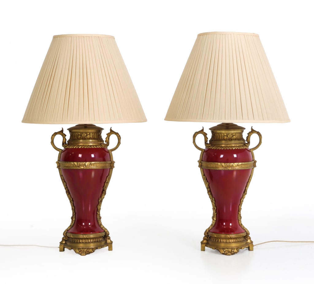 PAIR FRENCH GILT ORMOLU PORCELAIN URN TABLE LAMPS: Gilt bronze mounted red porcelain urn table lamps. Each baluster-form body in red glaze, mounted with gilt bronze collars, twin scroll handles, and foliate swags, raised on plinth bases. France, Late
