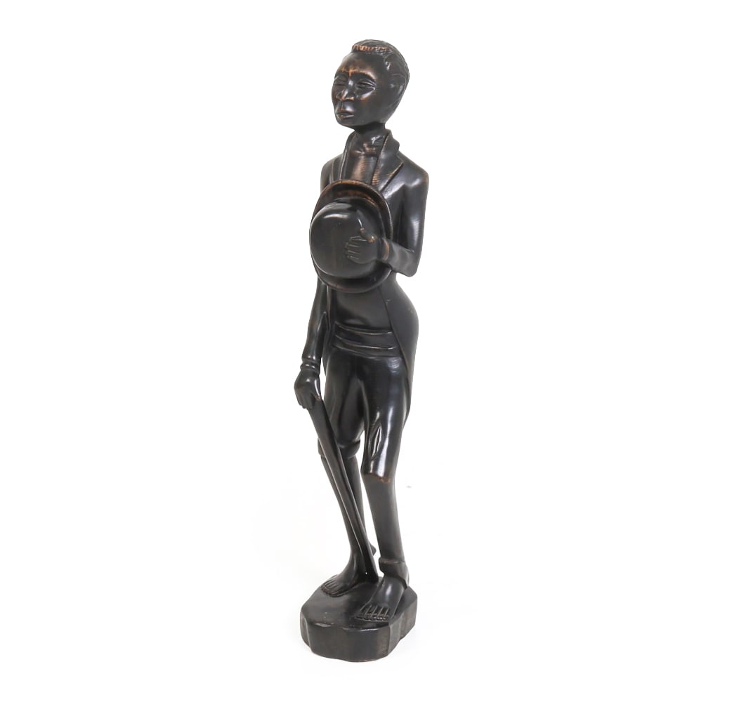 E. SIMEON (HAITIAN) CARVED WOOD FIGURE SCULPTURE: Haitian folk art sculpture, featuring a man in formal attire holding a bowler hat and a stick. Signed under base. Dimensions: H 35" x W 6.5" x D 7" Condition: Wear consistent with age and use. Stress