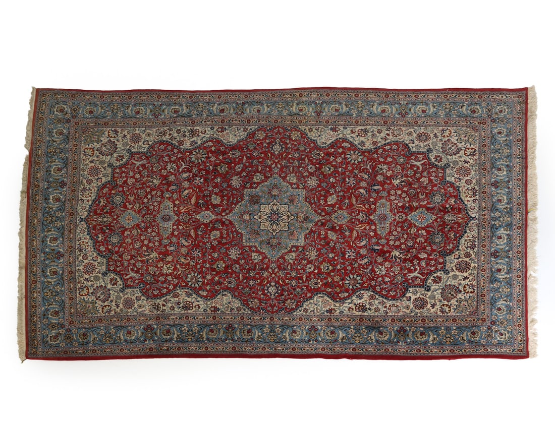 PERSIAN KASHAN RUG: Persian Kashan rug featuring a prominent central medallion and intricate floral patterns surrounding, using blue red and yellow. With fringe edges. Dimensions: L 144" x W 91" Condition: Spots of