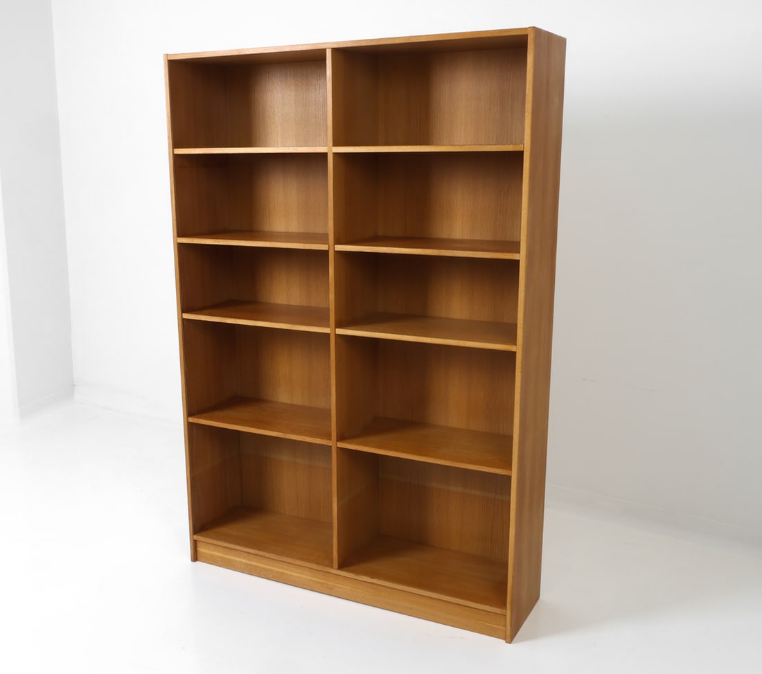 STYLE OF BORGE MOGENSEN DANISH OAK BOOKCASE 1960S: Adjustable shelves on plinth base. Denmark, circa 1960s. Dimensions: H 69" x W 47" x D 12.5" Condition: Wear consistent with age and use. Scuffs and rubs. Loss to veneer at edges.