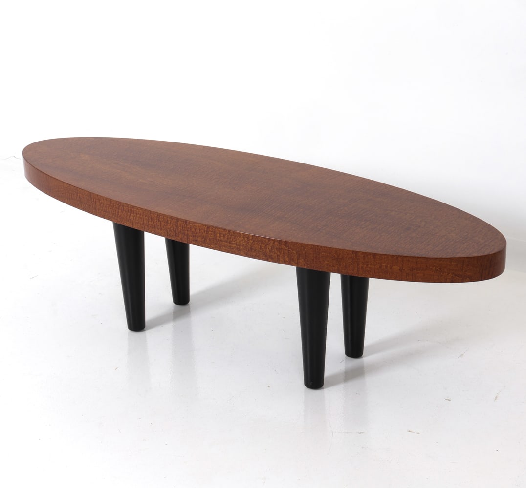 GILBERT ROHDE STYLE MAHOGANY COFFEE TABLE: Flame mahogany veneer coffee table with high-gloss lacquer finish and black wooden legs. 20th c. Dimensions: H 18.25" x W 60" x D 20" Condition: Wear consistent with age and use, including faint rubs