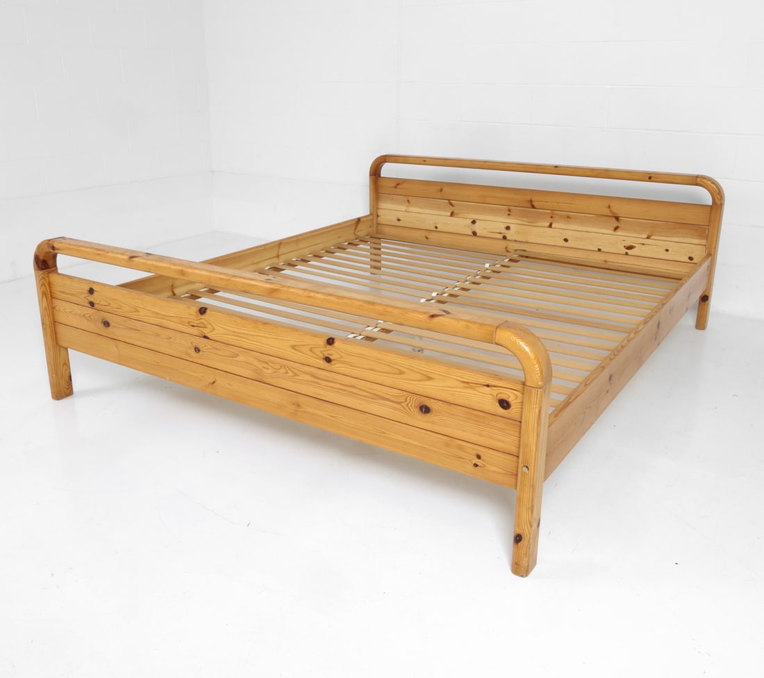 STYLE OF DAUMILLER DANISH PINE BED FRAME C. 1970S: Danish king size bed frame made of pine featuring rounded head and footboard with bed slats. Apparently unmarked. Denmark, circa 1970s. Dimensions: H 26" x W 69" x D 83" (Inside) W 67" x D 79"