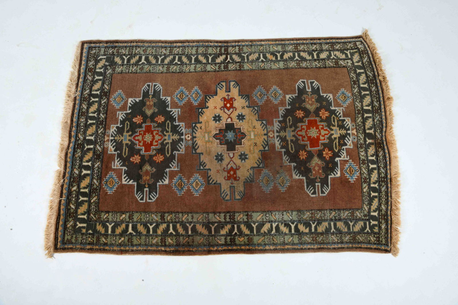 HAND-KNOTTED TURKISH WOOL RUG: Hand-woven wool rug with brown, green, and red geometric decoration. 20th century. Dimensions: L 80" x W 53" Condition: Slight sun fading. Wear consistent with age and use.