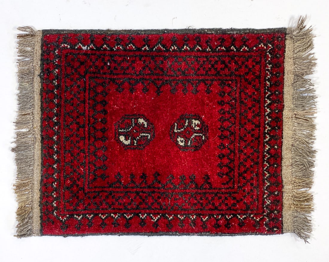 HAND-KNOTTED AFGHAN BOKHARA WOOL RUG: Hand-woven wool rug with red and navy geometric 'guls' designs. Mid 20th century. Dimensions: L 27" x W 19.5". Condition: Minor fraying and fading, wear consistent with age and use.