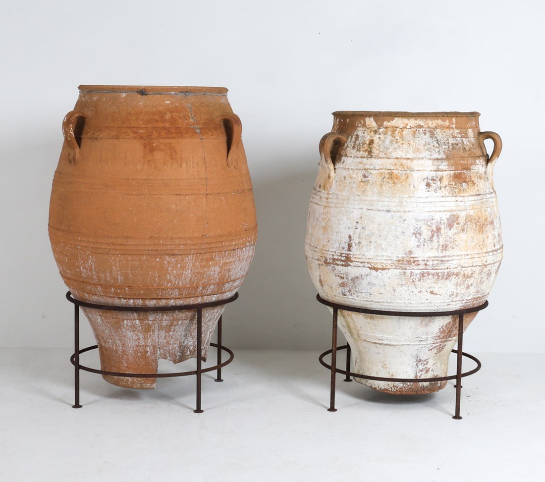PAIR ANTIQUE MEDITERRANEAN TERRACOTTA OLIVE JARS: Large terracotta olive jars in wrought iron stands. Mediterranean, circa 19th century. Dimensions: Tallest H 47" x Dia. 28.5". Condition: Losses to lower ends. Scuffs, scratches, and few previous repa