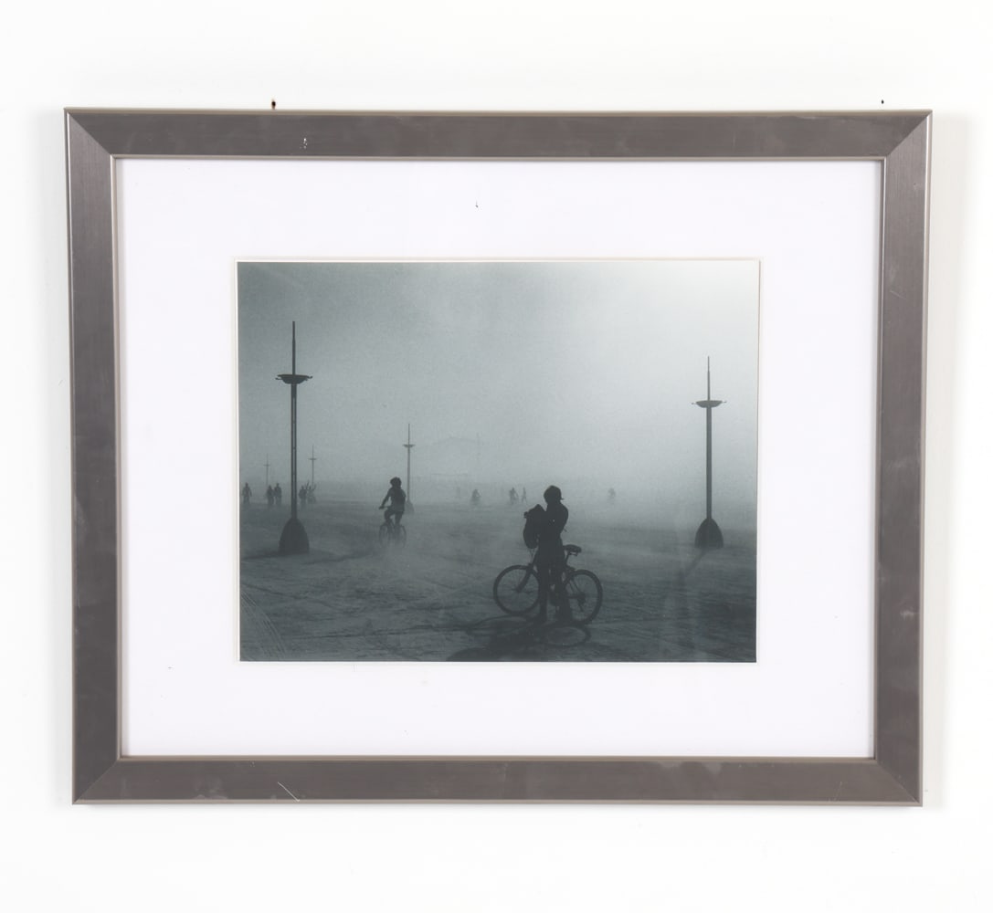 LUCAS SHEIN BURNING MAN PHOTOGRAPH: Moody photograph showing figures on bikes. Dimensions: Frame H 18" x W 22". Photo H 10.5" x W 13.5". Condition: Photo slightly askew in frame. Few minor scratches to frame.