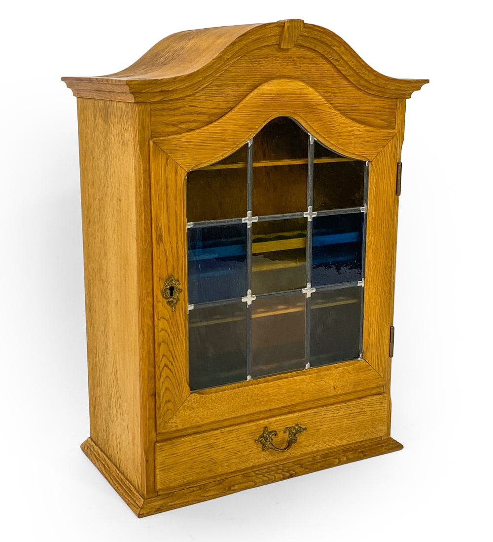 DANISH OAK & GLASS WALL MOUNTED CABINET C. 1970S: Key included. Oak hanging wall cabinet fitted for pipes with stained glass to cabinet door. (1) Drawer. Denmark, circa 1970s. Dimensions: H 28.5" x W 20" x D 11.25". Condition: Minor scuffs and dings.