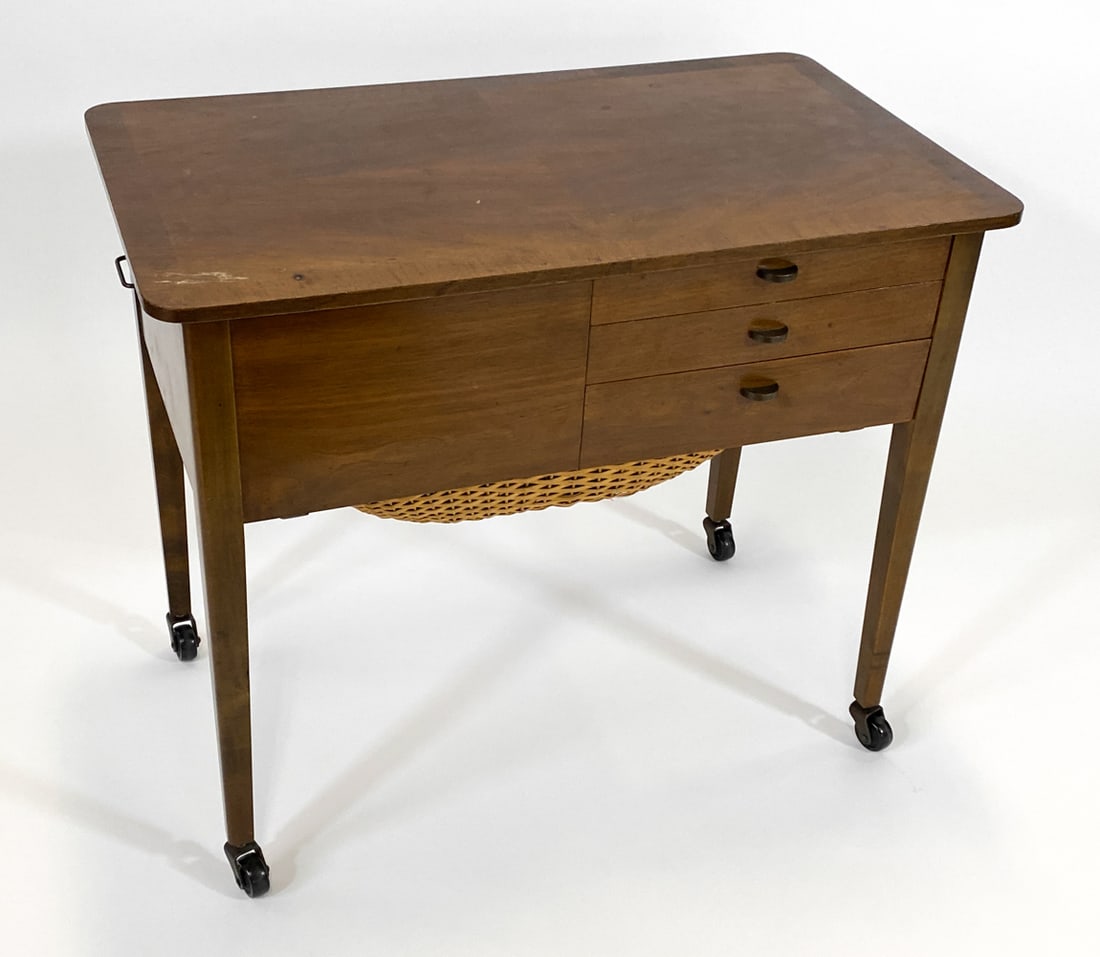 ATTR AMAGER BOLIGHUS WALNUT SEWING TABLE 1970S: Walnut sewing chest with rattan basket drawer on casters. Brass pulls. Apparently unmarked. Denmark, circa 1970s. Dimensions: H 25" x W 29" x D 17". Condition: Minor losses to veneer under top around